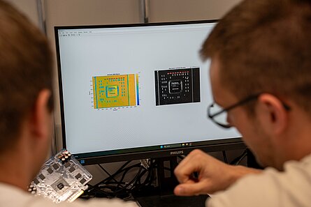 zwei Studierende arbeiten an einem Bildschirm, der zwei aufbereitete Aufnahmen von Chips in einer Bildverarbeitungssoftware darsrtellt