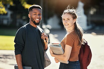 Students, couple or university friends walking together with books for education and learning on campus with scholarship. Portrait of an interracial man and woman together on college or school ground